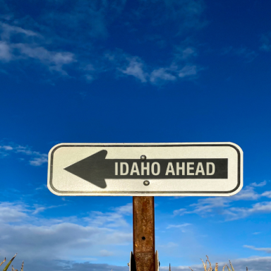 Signpost indicating "Idaho Ahead" with a left-pointing arrow against a blue sky.